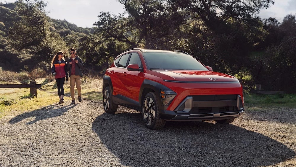 Two hikers walking toward a red 2026 Hyundai Kona parked by a trail
