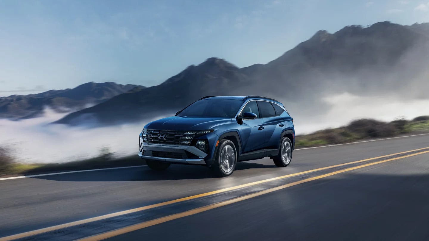 A blue Hyundai Tucson driving on a road in a mountain range