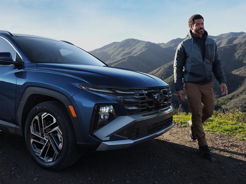 A person walking beside a blue 2026 Hyundai Tucson SUV with mountains in the background