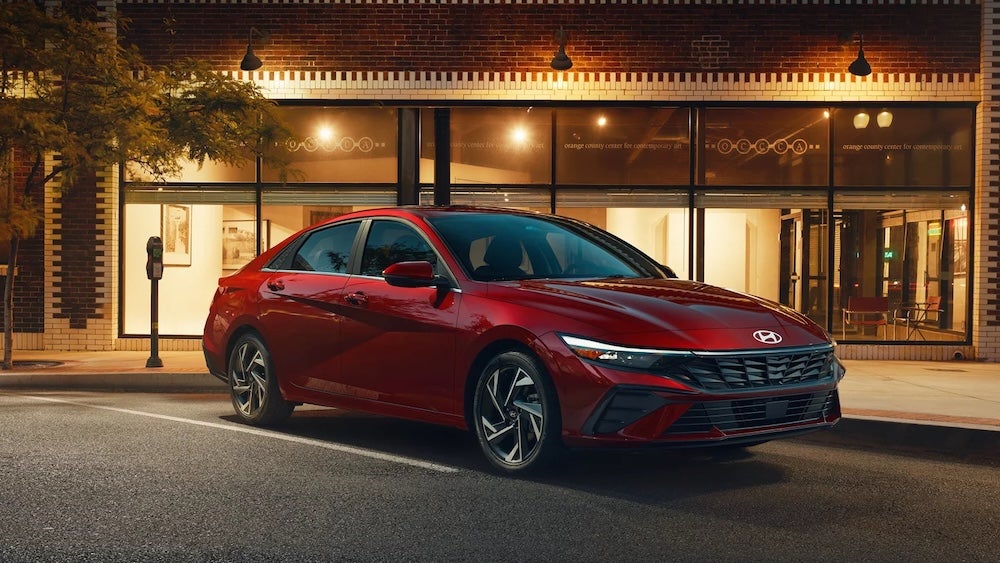 A red 2026 Hyundai Elantra sedan parked outside an art gallery at night