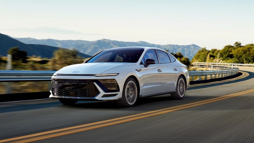A white Hyundai Sonata sedan driving down a curving road