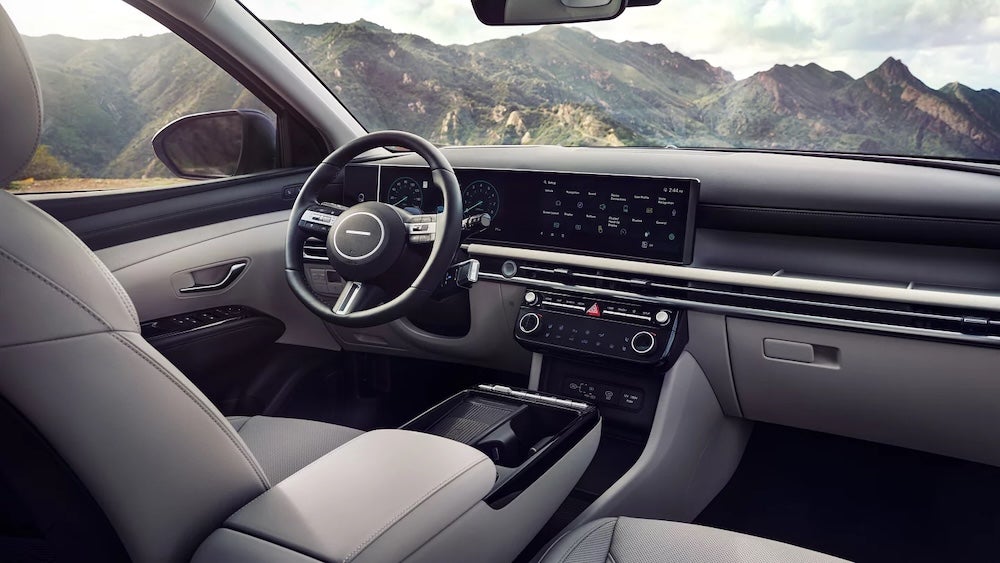 The front seat, steering wheel, and dash of a 2026 Hyundai Tucson SUV, with mountains visible through the windshield
